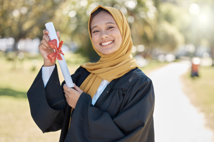 International female graduate holding a diploma on a university campus.