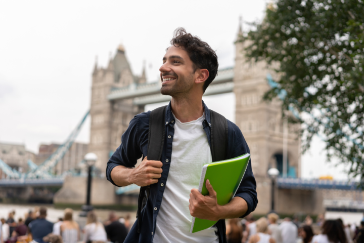 International student holding books near Tower Bridge in London, representing studying in the UK